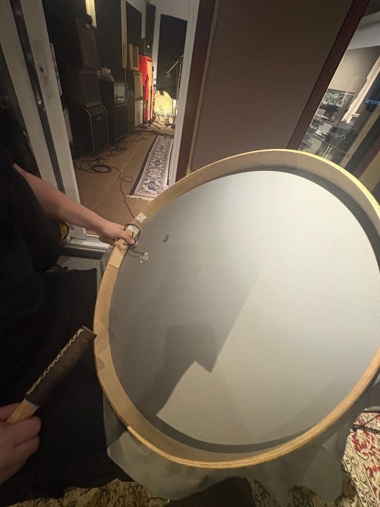 A finished traditional Inuit frame drum held up in a studio, with a Cortado Xe mounted just above the handle