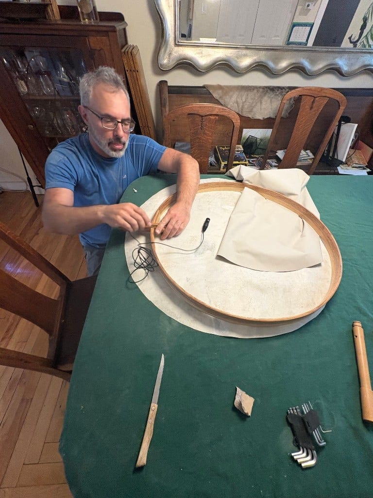 Lacing the drumhead onto the bent-wood frame at the workbench